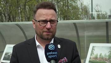 Piotr Gacek, mężczyzna w garniturze i okularach, trzyma mikrofon Polsat Sport.