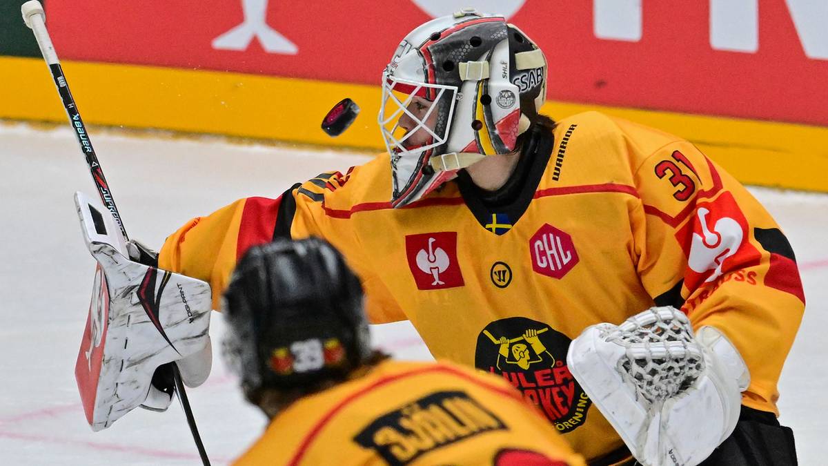 Bramkarz w żółtym stroju hokejowym z numerem 30 na plecach, z maską na twarzy i rękawicami bramkarskimi, w akcji na lodowisku.