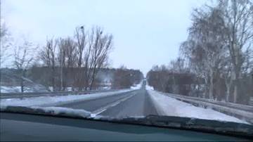 Droga pokryta śniegiem i lodem, z widocznymi drzewami po bokach i niebem w tle.