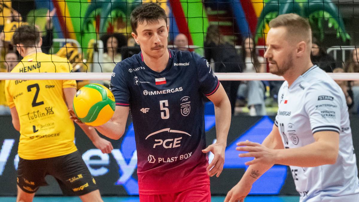 Siatkarz PGE Projekt w granatowej koszulce z numerem 5 trzyma piłkę, obok niego drugi zawodnik w białej koszulce