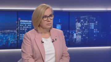 Kobieta w różowym żakiecie siedzi na tle nocnego miasta, patrząc przed siebie.