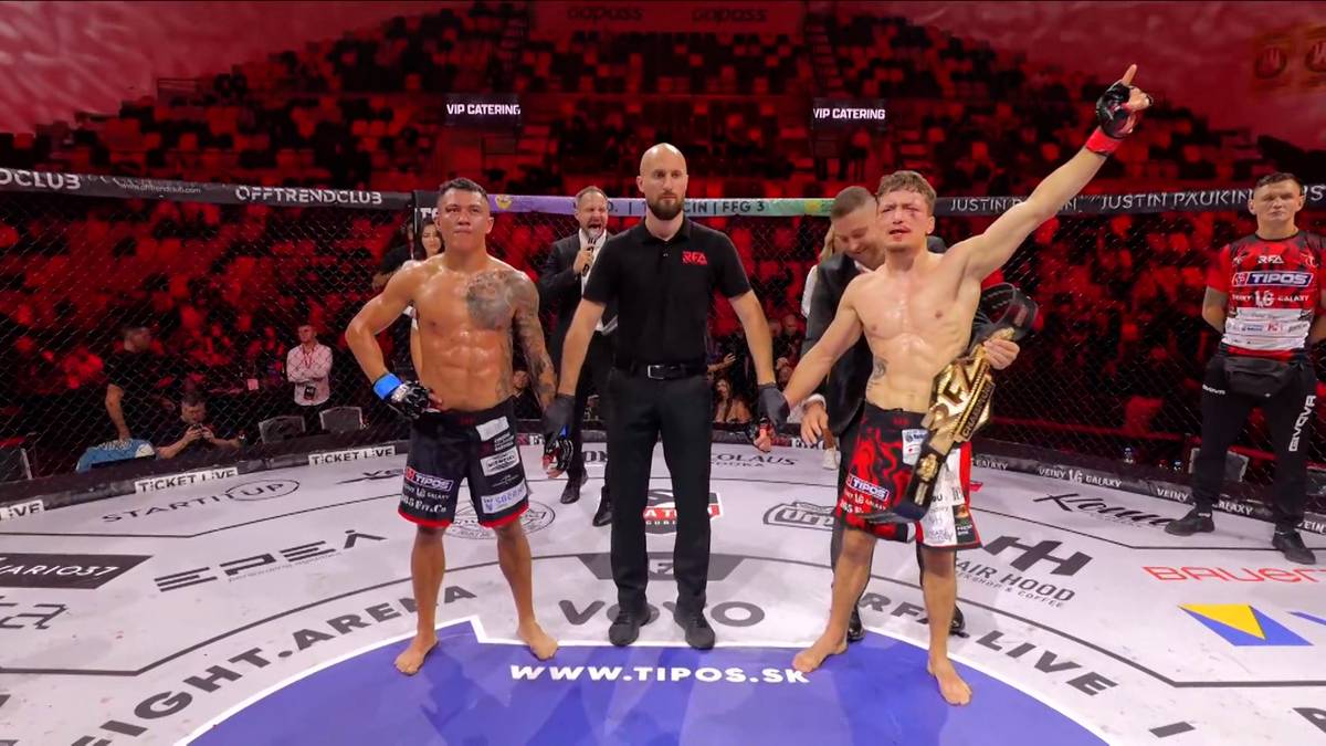 Dw&oacute;ch zawodnik&oacute;w MMA i sędzia stoją na środku ringu. Jeden z zawodnik&oacute;w unosi rękę w geście zwycięstwa, trzymając pas mistrzowski.