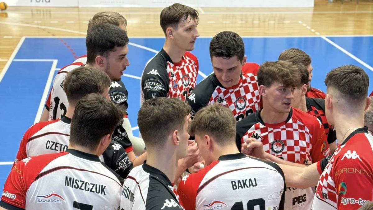 Grupa siatkarzy w czerwono-białych strojach sportowych stoi w kręgu.