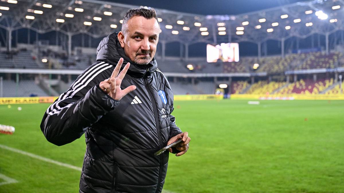 Trener piłkarski na stadionie pokazujący trzy palce.