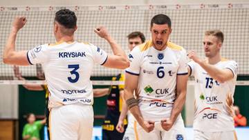 Siatkarze w białych strojach z numerami na koszulkach unoszą ręce w geście radości po udanej akcji podczas meczu.