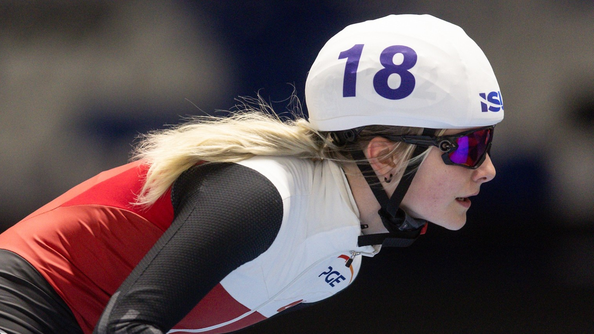 Łyżwiarka szybka w białym kasku z numerem 18 i biało-czerwonym stroju, w pozycji startowej na lodzie.