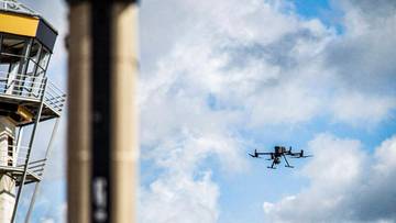 Dron w locie na tle wieży kontrolnej i drzew.