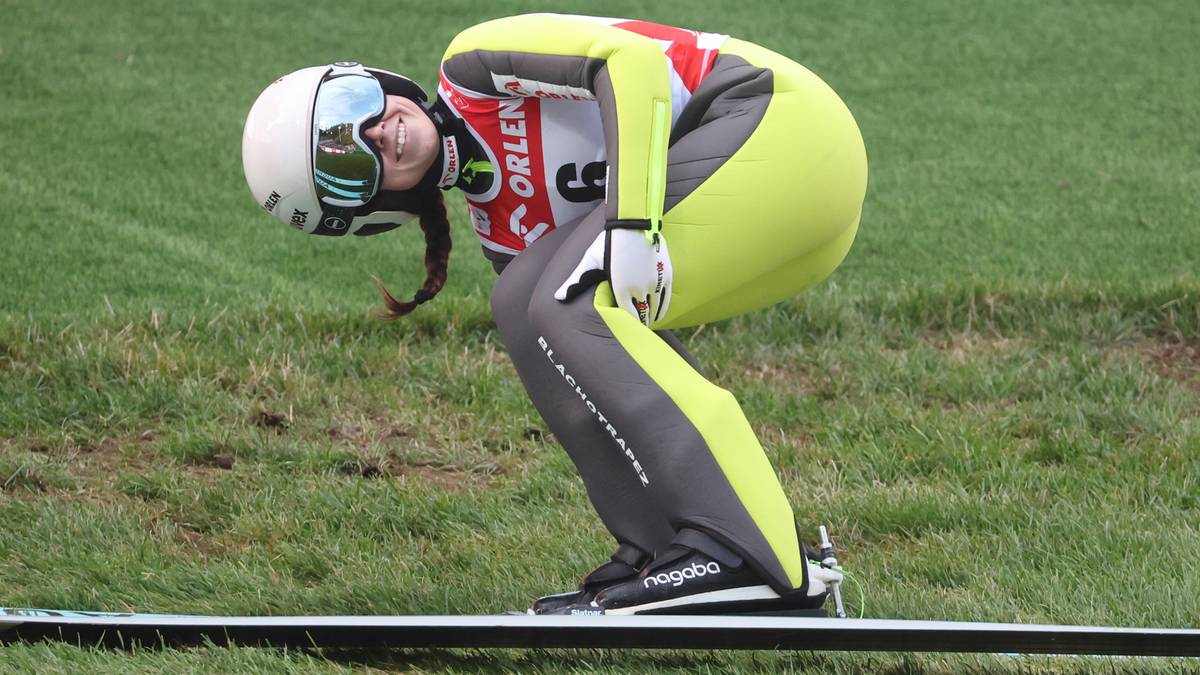 Zawodniczka w ż&oacute;łtym i szarym kombinezonie narciarskim, białym kasku i goglach, w pozycji startowej na nartach.