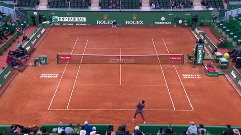 Tenisiści rozgrywają mecz na ceglanym korcie w Monte Carlo. Jedna z postaci, Ugo Humbert, jest w trakcie uderzenia piłki.