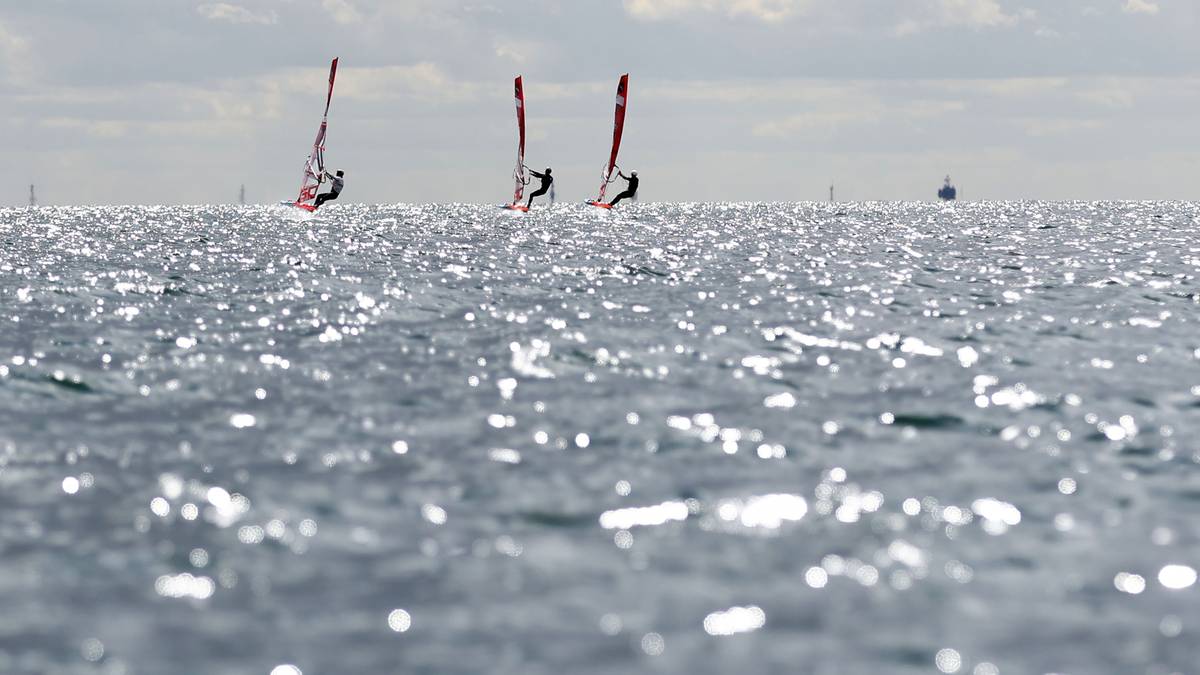 Trzej windsurferzy płynący na deszczu refleksów świetlnych po morzu pod zachmurzonym niebem.