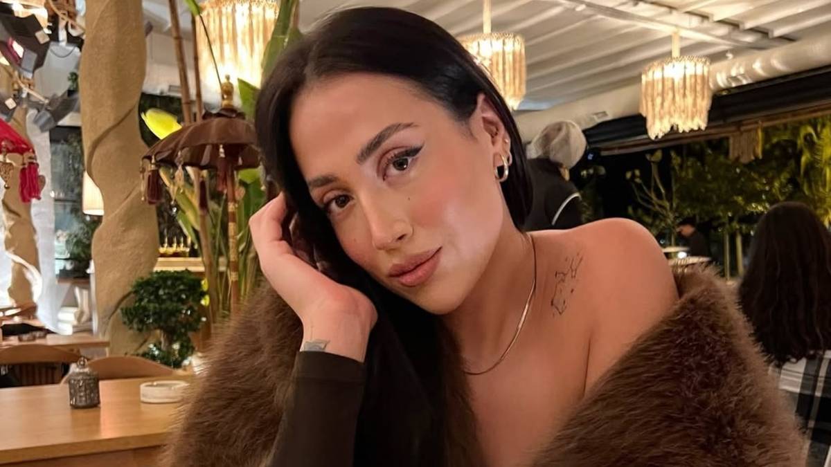 Kobieta w brązowym futrze z dłonią na policzku.