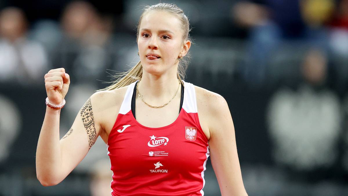 Zawodniczka tenisa w czerwonej koszulce, z uniesioną zaciśniętą pięścią, na tle rozmytej widowni.