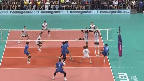 Siatkarz w białej koszulce skacze do ataku nad siatką, z piłką w ręku, w trakcie meczu siatk&oacute;wki.