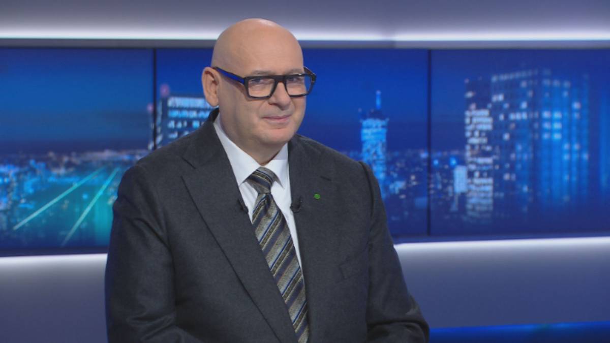 Piotr Zgorzelski w garniturze i okularach siedzi w studiu telewizyjnym.