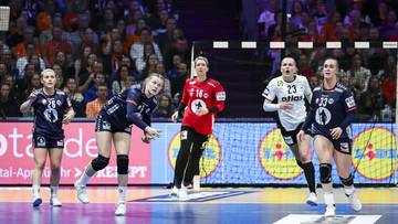 Pięć zawodniczek w strojach sportowych gra w piłkę ręczną na boisku przed widownią.