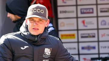 Młody mężczyzna w czapce z daszkiem i kurtce sportowej patrzy prosto przed siebie.