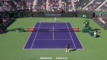 Kort tenisowy podczas meczu, z dwoma zawodnikami na korcie i widownią na trybunach. Napis "INDIAN WELLS" widoczny na nawierzchni.