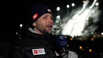 Mężczyzna w czapce z flagą Polski i logo "4F", rozmawia do mikrofonu z logo "Polsat Sport". W tle widać oświetloną skocznię narciarską.