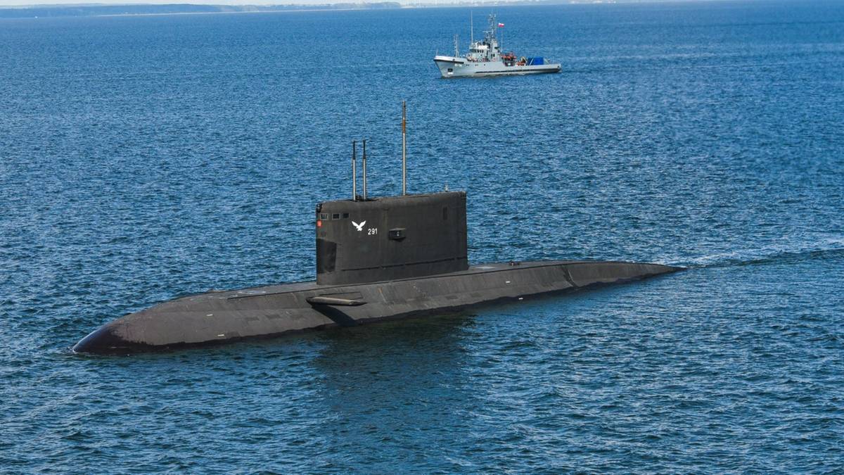 Okręt podwodny płynący po wodzie, z mniejszym statkiem na horyzoncie.