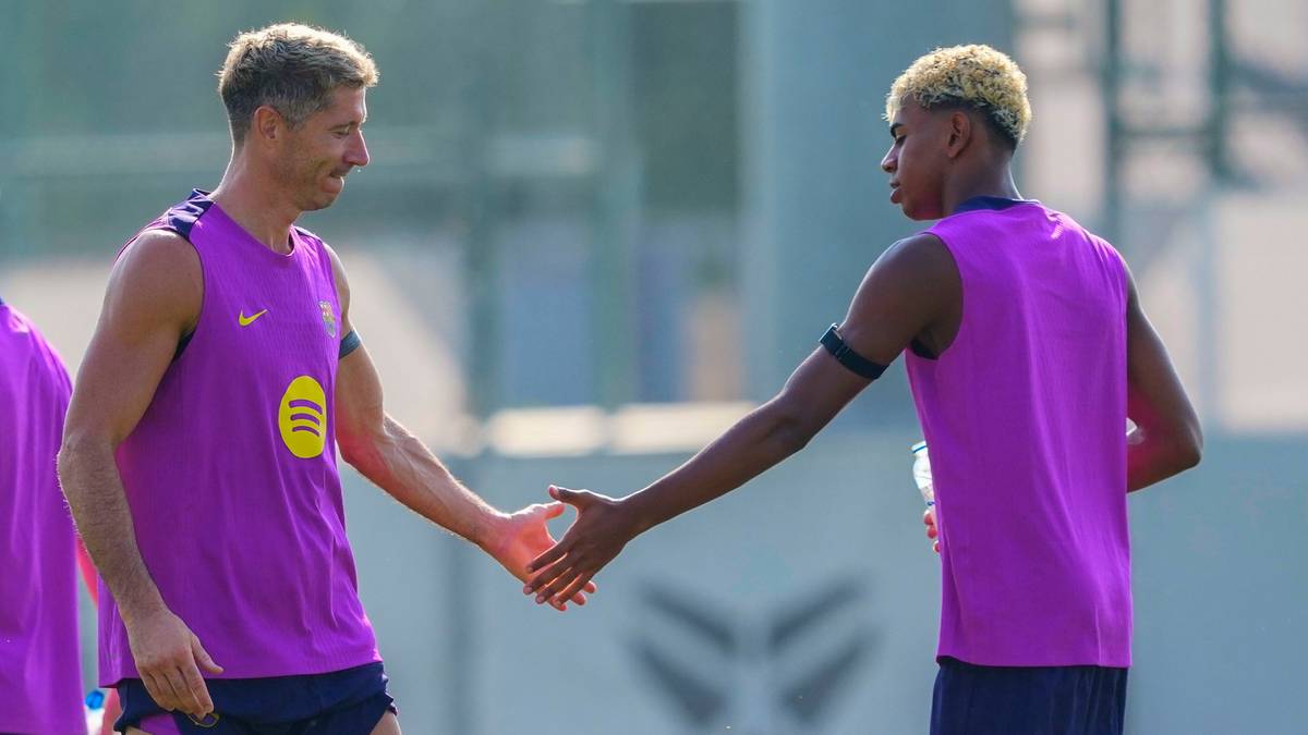 Piłkarz Robert Lewandowski i młody zawodnik FC Barcelony podają sobie ręce na boisku treningowym.