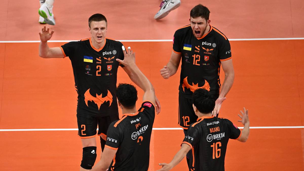 Siatkarze w czarnych strojach z pomarańczowymi detalami świętują zwycięstwo. Dwóch zawodników podnosi ręce, jeden z nich wykonuje gest "piątki". Na koszulkach widoczne numery i nazwy drużyn.