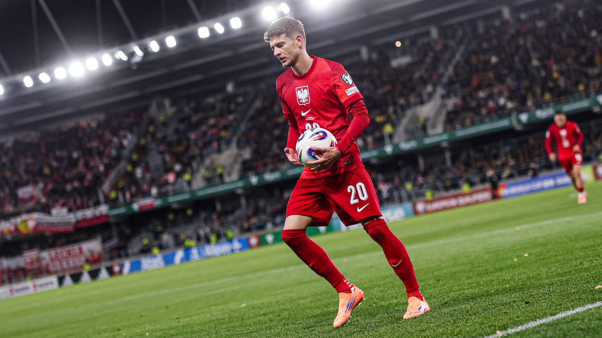 Piłkarz w czerwonej koszulce reprezentacji Polski z numerem 20 na plecach biegnie z piłką po boisku.