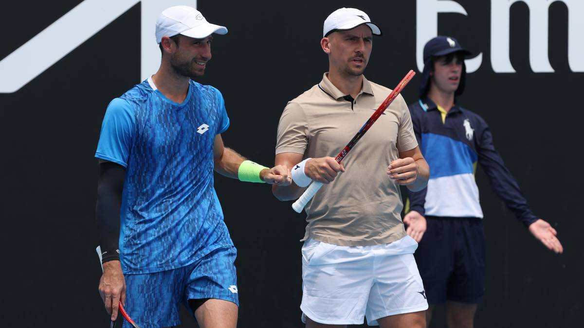 Dwóch tenisistów w strojach sportowych stoi obok siebie, jeden trzyma rakietę, drugi ma rękę na ramieniu pierwszego.