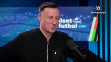 Tomasz Hajto w czarnej kurtce, siedzący w studiu telewizyjnym. W tle logo Polsat Sport i napisy związane z piłką nożną.