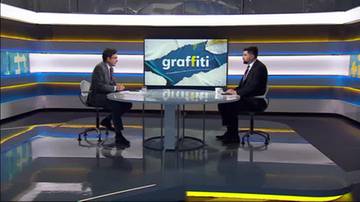 Dw&oacute;ch mężczyzn siedzi przy stole w studiu telewizyjnym, przed ekranem z napisem "graffiti".
