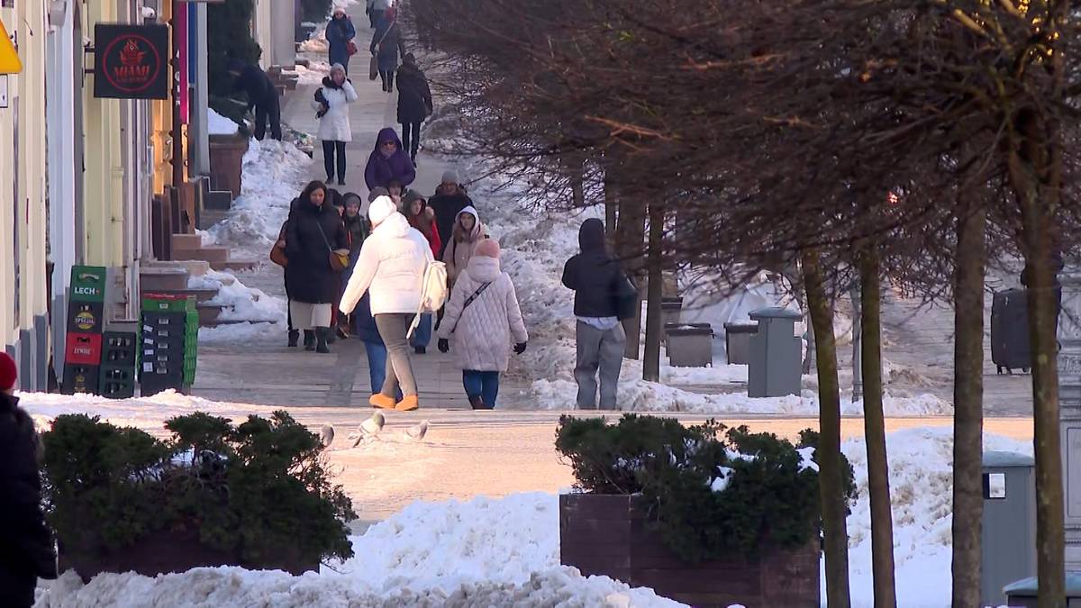 Ulica pokryta śniegiem z ludźmi spacerującymi w zimowej scenerii.