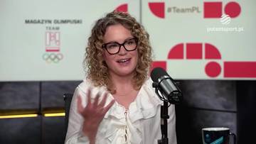 Kobieta z kręconymi włosami i okularami, siedząca przed mikrofonem w studiu telewizyjnym.