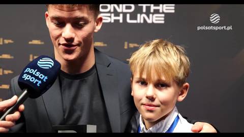 Młody mężczyzna trzymający mikrofon Polsat Sport obok młodego chłopca.
