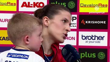 Kobieta siatkarka w zbliżeniu, patrząca w prawo, m&oacute;wiąca do mikrofonu. Obok niej stoi mały chłopiec.