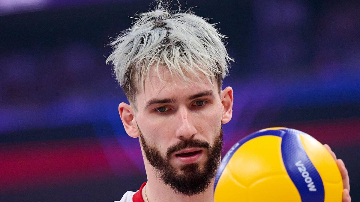 Siatkarz z jasnymi włosami i brodą trzymający piłkę siatkową.
