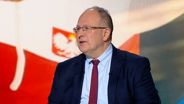 Marian Kmita w garniturze i krawacie, na tle polskiej flagi.