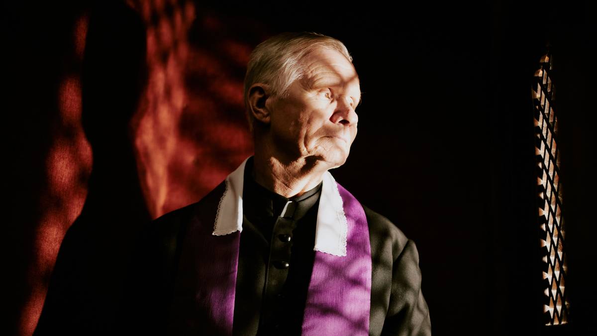 Starszy mężczyzna w sutannie z fioletową stułą, wpatrzony w bok.