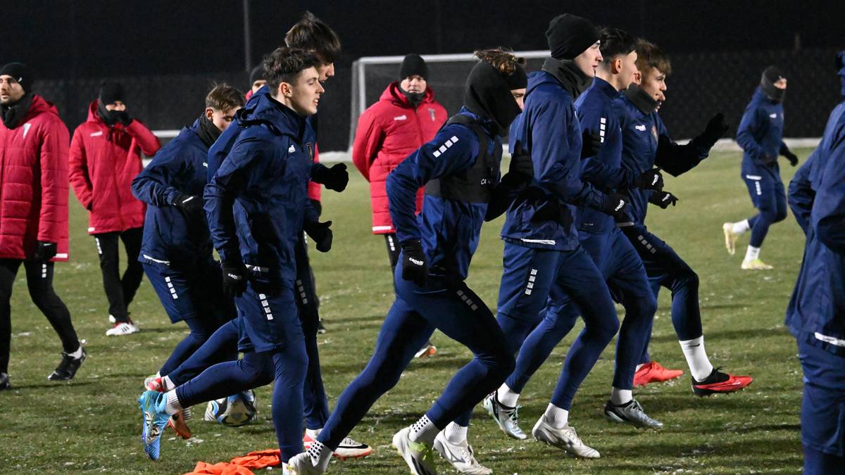 Grupa piłkarzy w granatowych strojach treningowych biegnie po boisku piłkarskim.