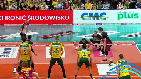 Zawodnicy drużyny siatkarskiej w akcji podczas meczu, jeden z nich wykonuje zagranie z piłką.