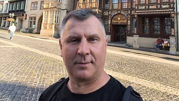 Portret mężczyzny na tle zabytkowej ulicy z kamiennymi budynkami.