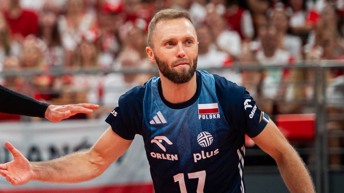 Trzech siatkarzy podczas meczu siatk&oacute;wki, dw&oacute;ch w czerwonych strojach, jeden w granatowym.