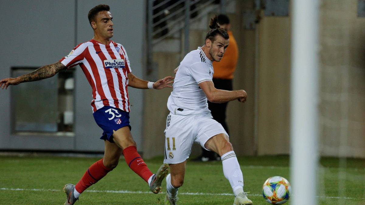 Dw&oacute;ch piłkarzy w akcji na boisku piłkarskim, jeden w białym stroju i jeden w czerwono-białe pasy.