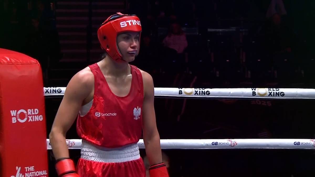 Młoda bokserka w czerwonym stroju i kasku wychodzi na ring.