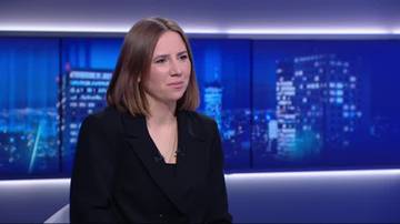 Anna Bryłka w czarnym żakiecie, z naszyjnikiem, siedzi przed niebieskim tłem z widokiem nocnego miasta.