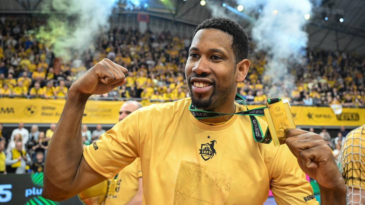 Siatkarz w żółtej koszulce z mistrzowskim złotym medalem na szyi, radośnie unosi zaciśniętą pięść, świętując zwycięstwo na tle publiczności.