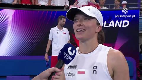 Iga Świątek w białej czapce i stroju sportowym udziela wywiadu z mikrofonem w ręce, z widoczną tablicą w tle.