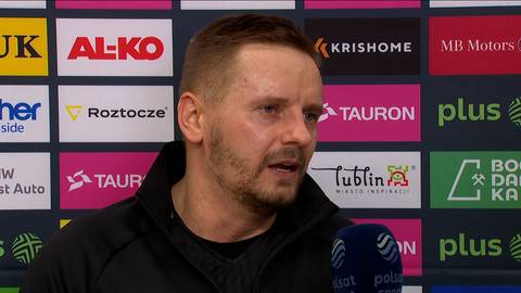 Damian Wojtaszek wypowiada się do mikrofonu na tle ściany ze sponsorami.