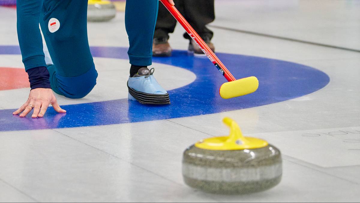 Gracz curlingu w pozie klęczącej z miotłą w dłoni, gotowy do rzutu kamieniem.