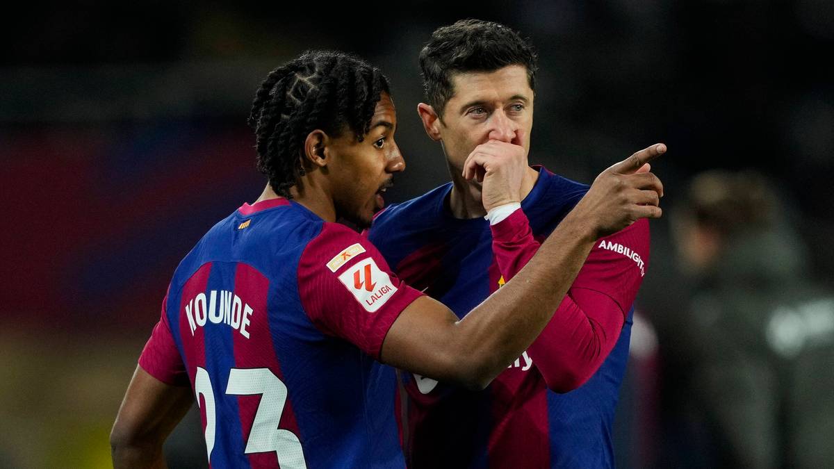 Dwóch piłkarzy FC Barcelona, jeden młody w niebiesko-czerwonym stroju z numerem 13 i nazwiskiem "YOUNDE", drugi starszy w tym samym stroju, rozmawia ze sobą na boisku.