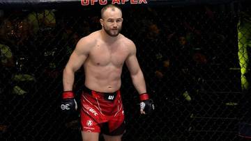Mężczyzna w czerwonych spodenkach UFC i rękawicach bokserskich stoi w oktagonie.