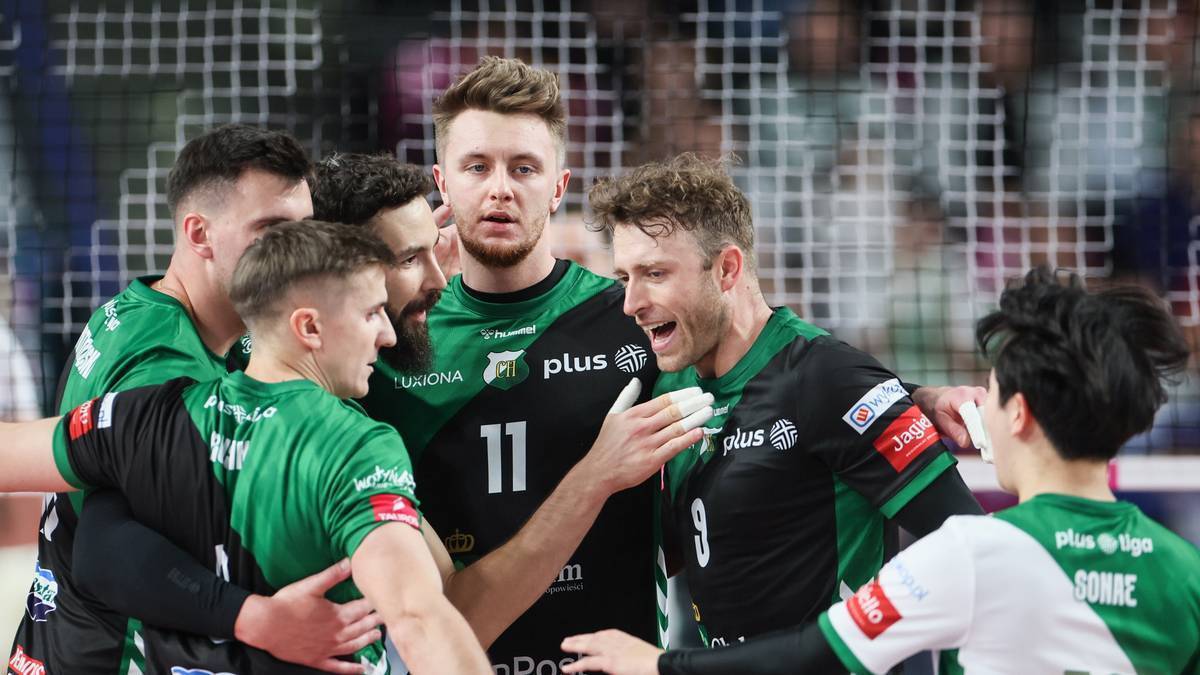 Grupa siatkarzy w zielono-czarnych strojach świętuje zwycięstwo, niekt&oacute;rzy się przytulają i rozmawiają.